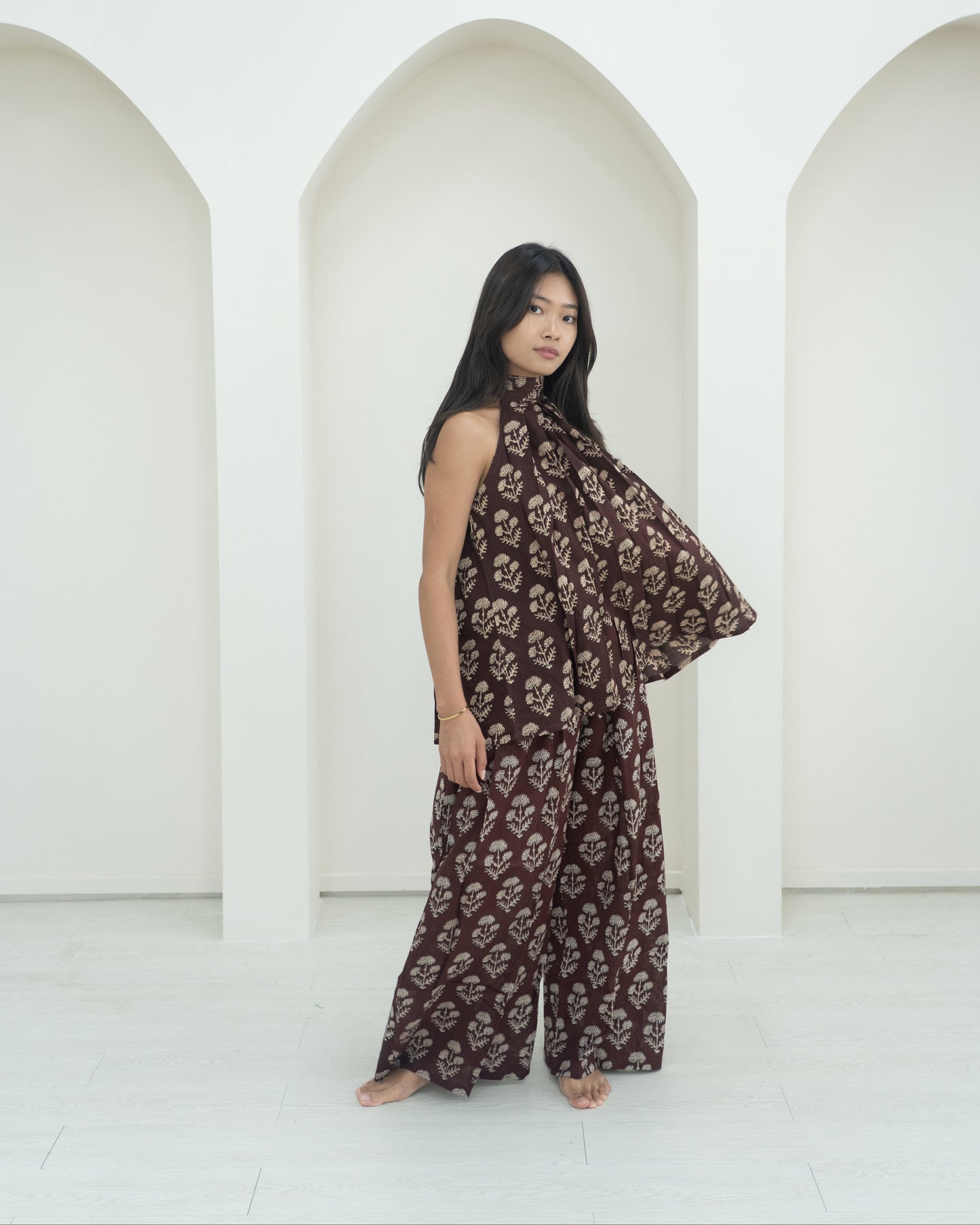 Woman wearing a brown floral outfit standing in front of white arches.