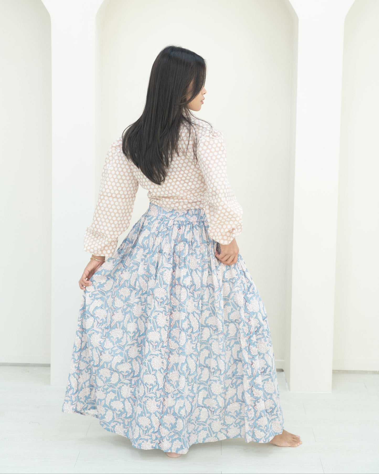 Woman wearing a white blouse with a blue floral skirt against a white background
