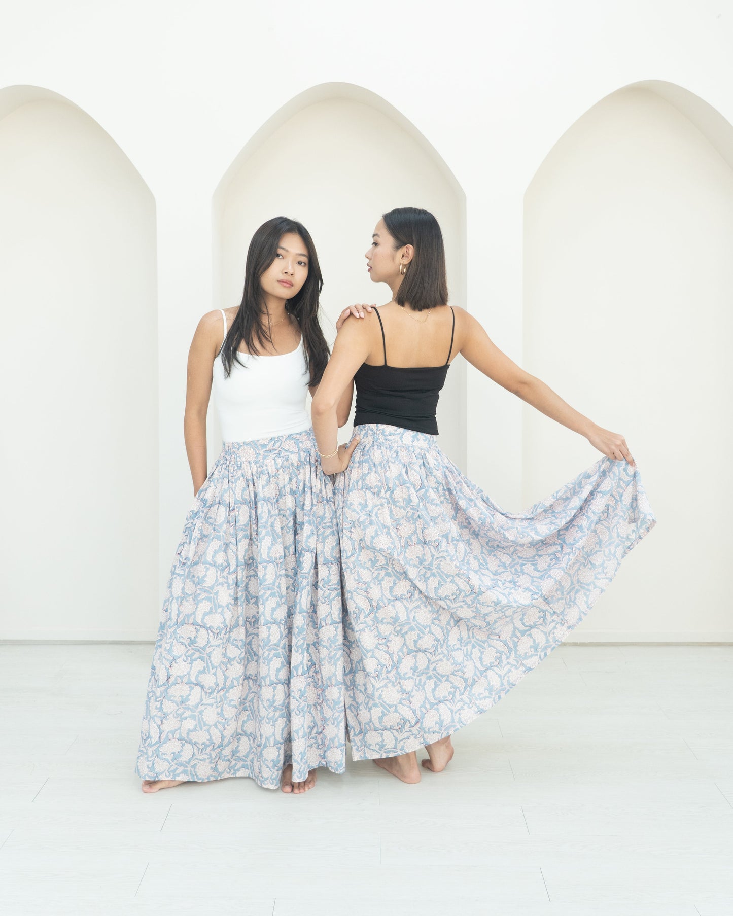 Two women standing in front of a white wall with a floral skirt.