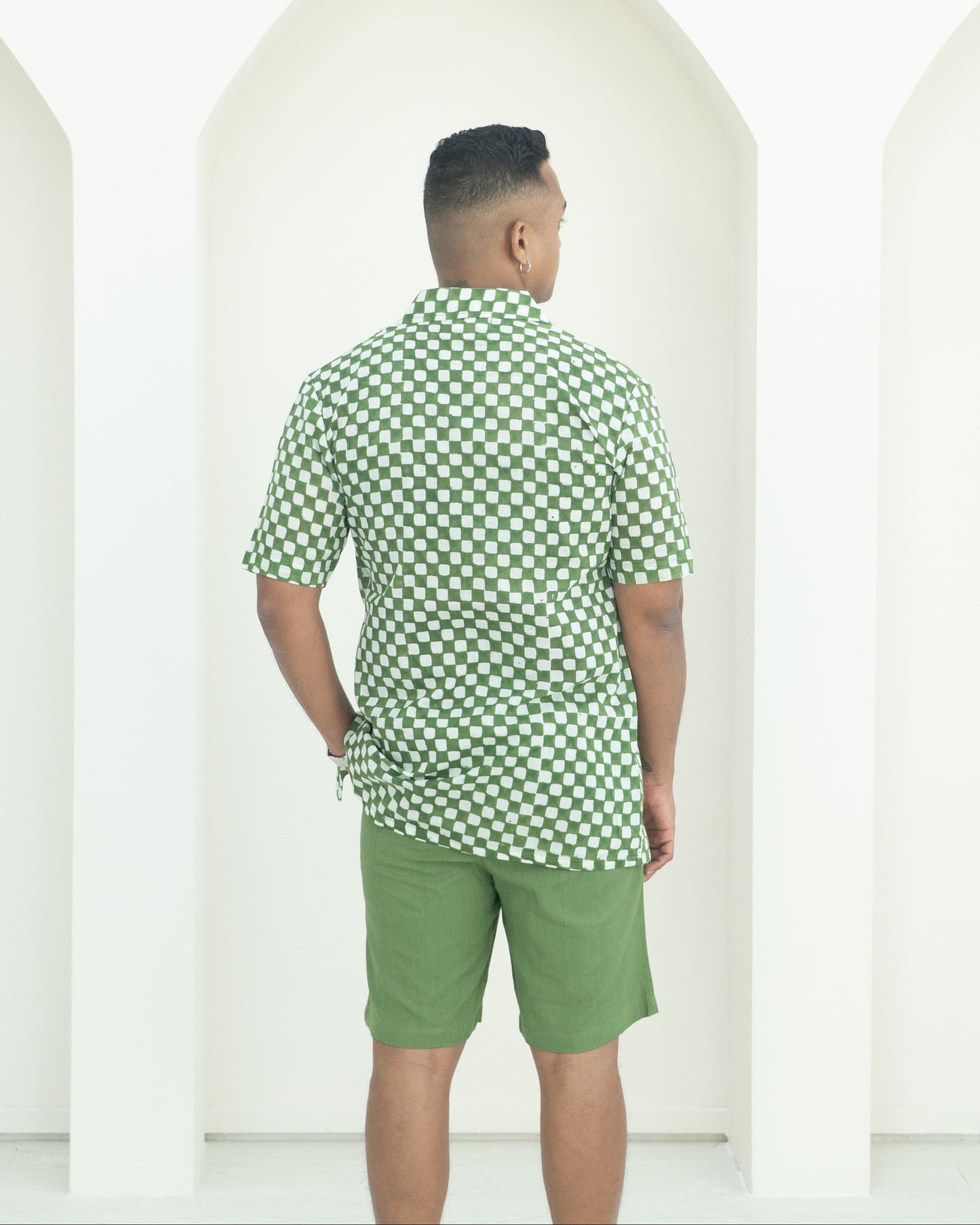 Man wearing a green checkered shirt and shorts standing against a white background
