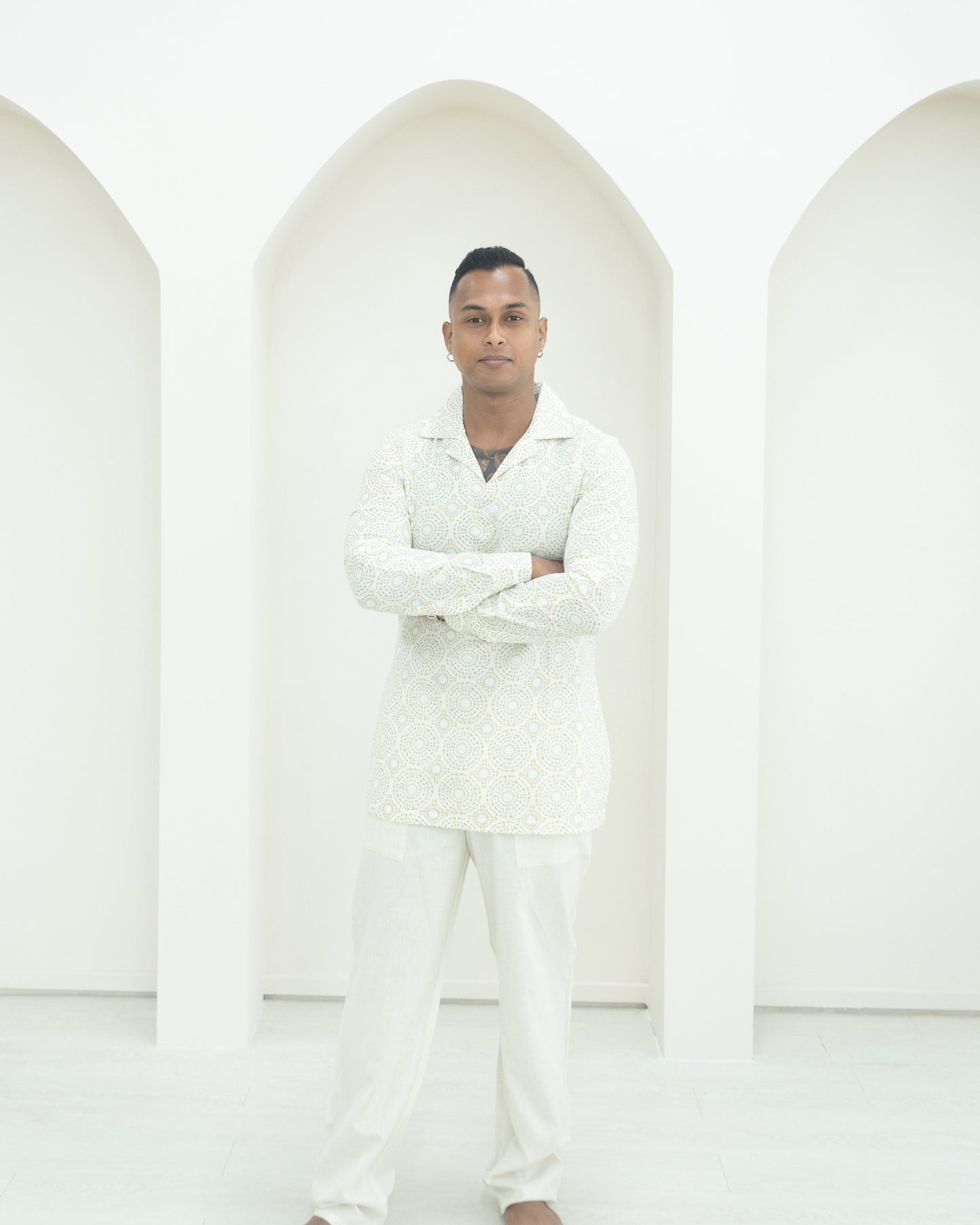 A man wearing a white patterned shirt and matching trousers.