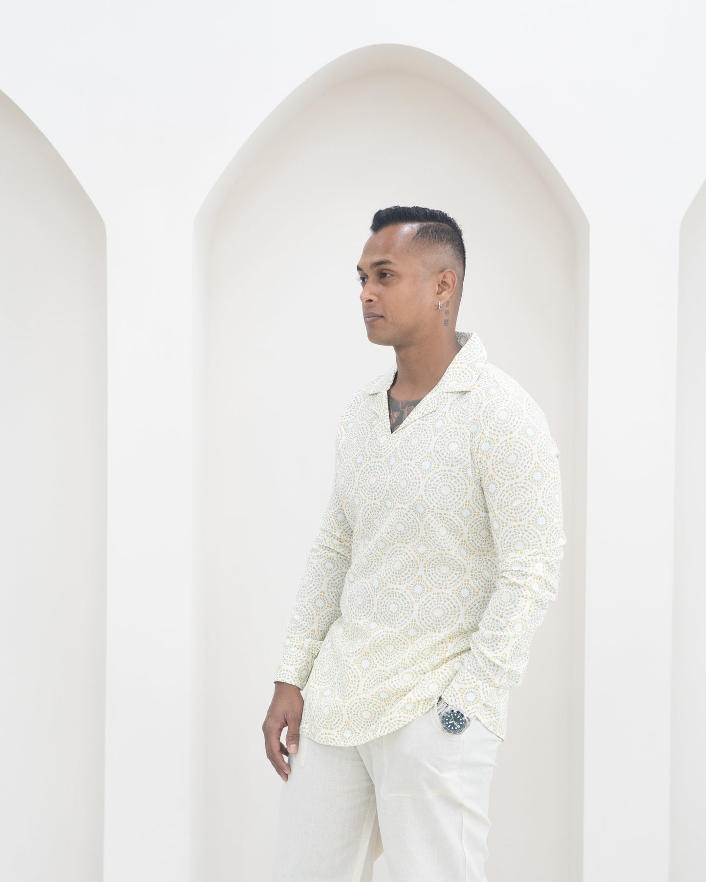 Man wearing a light-colored shirt and white pants against a white background