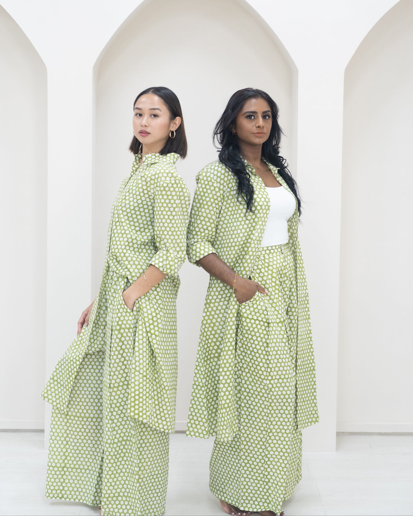 Two women wearing green polka dot outfits standing in front of white background