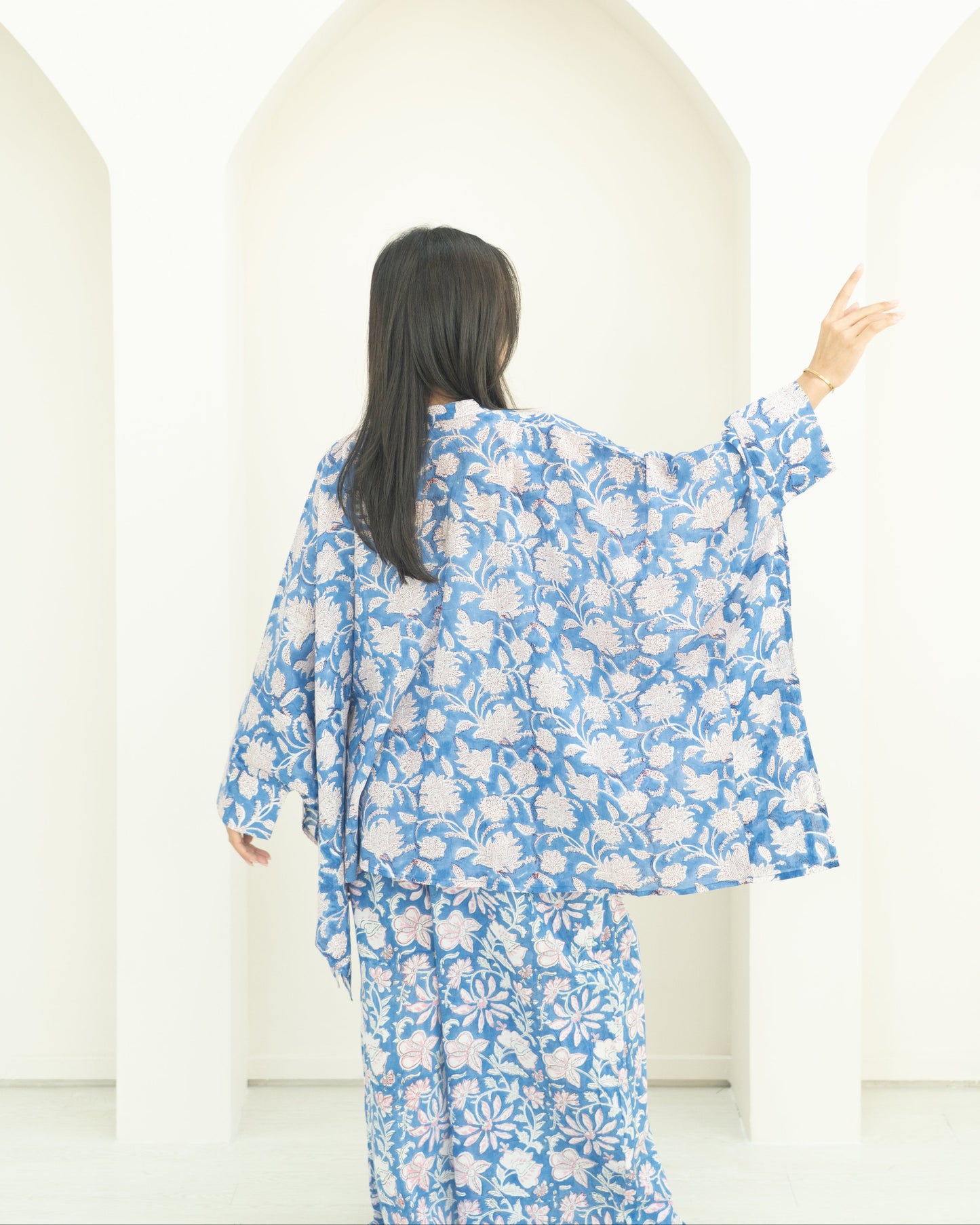Woman in a blue floral outfit standing in front of white background.