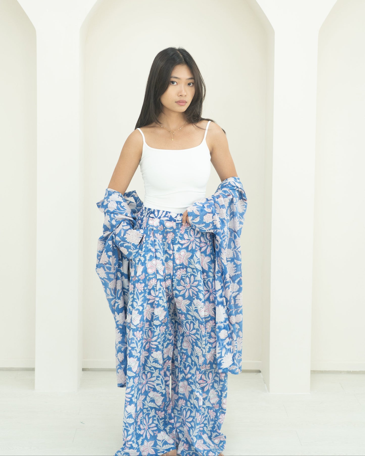 Woman wearing a white top and blue floral pants against a white background