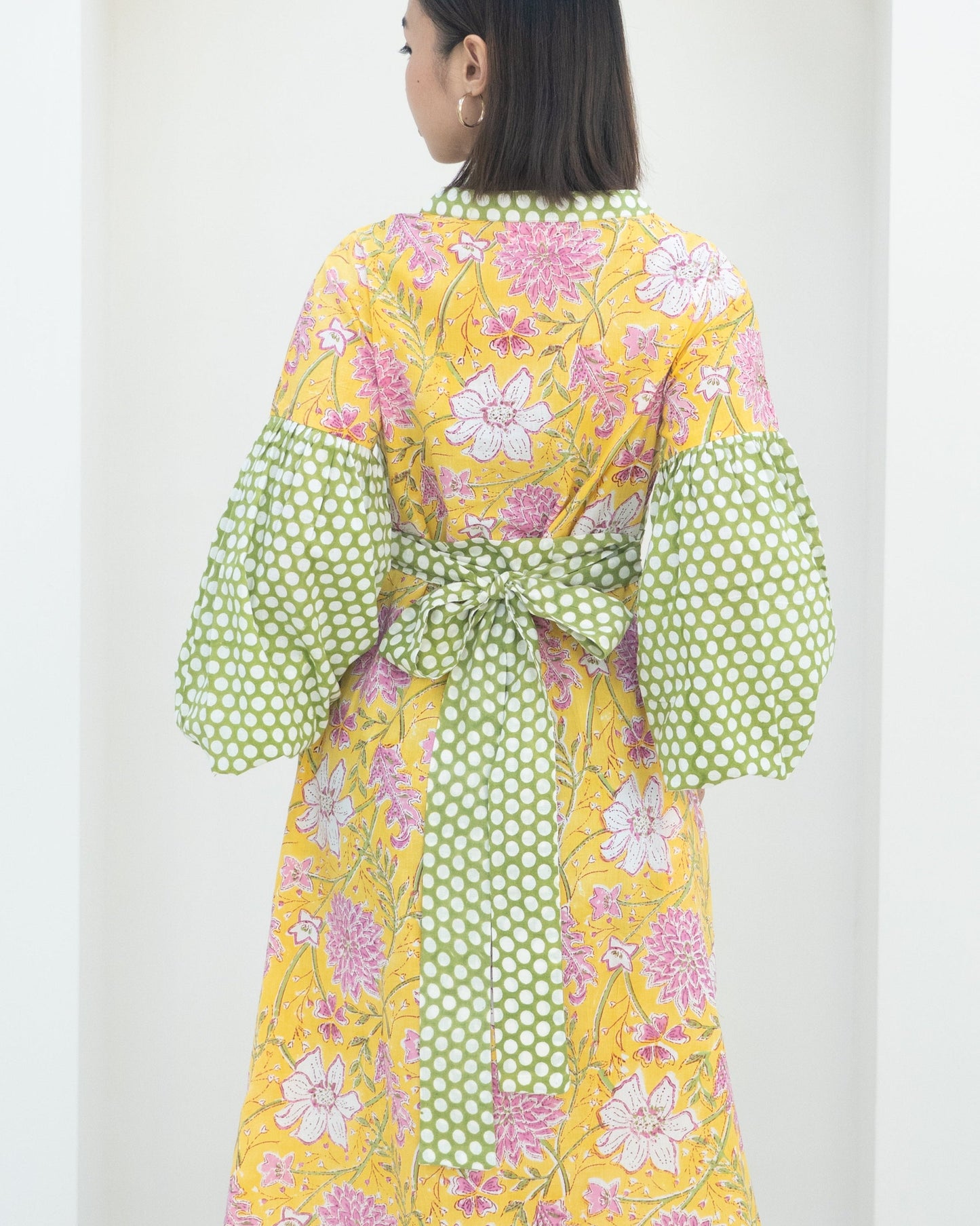 Woman wearing a colorful floral dress with polka dot sleeves on a white background
