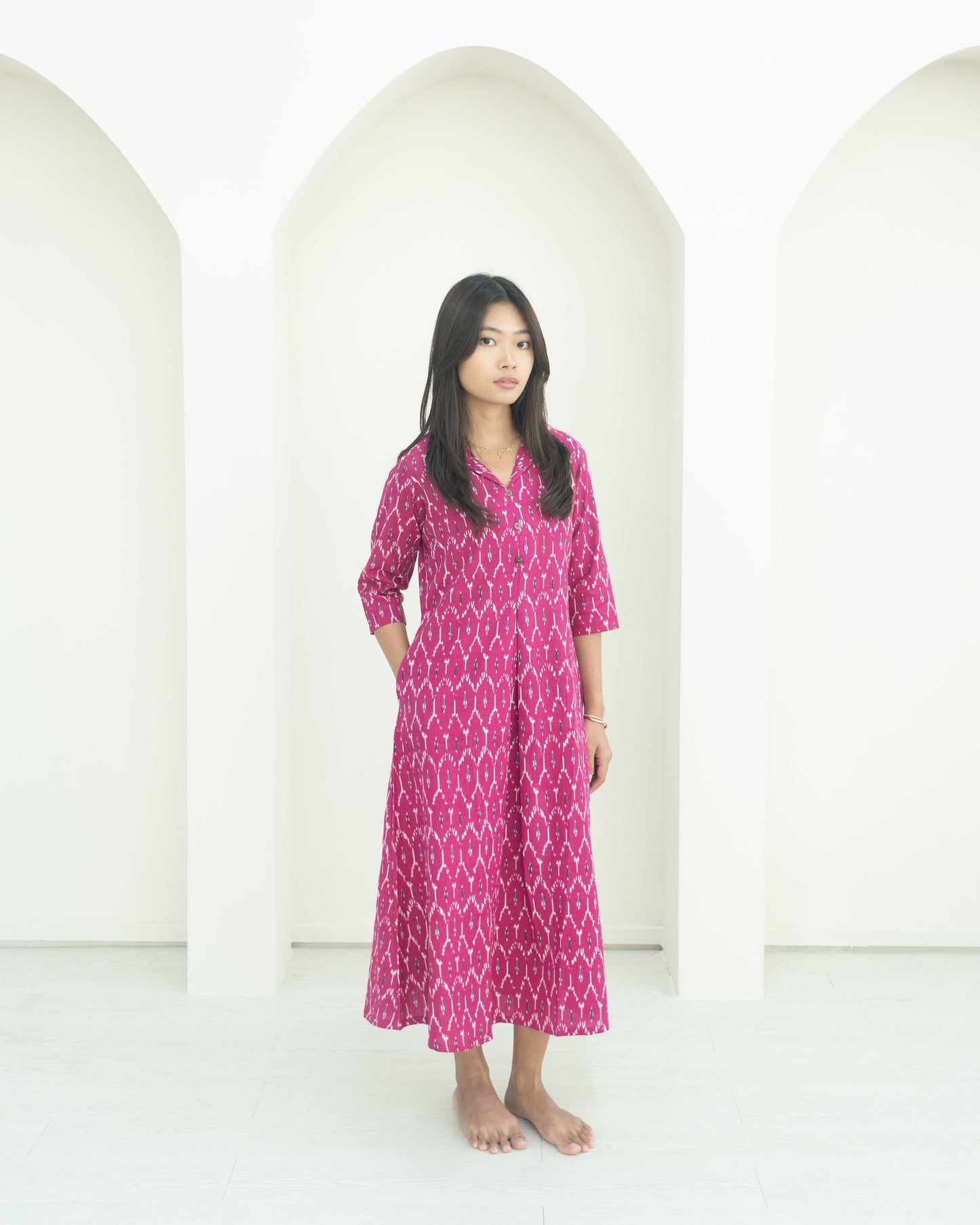 Woman wearing a pink patterned dress standing in front of white arches.