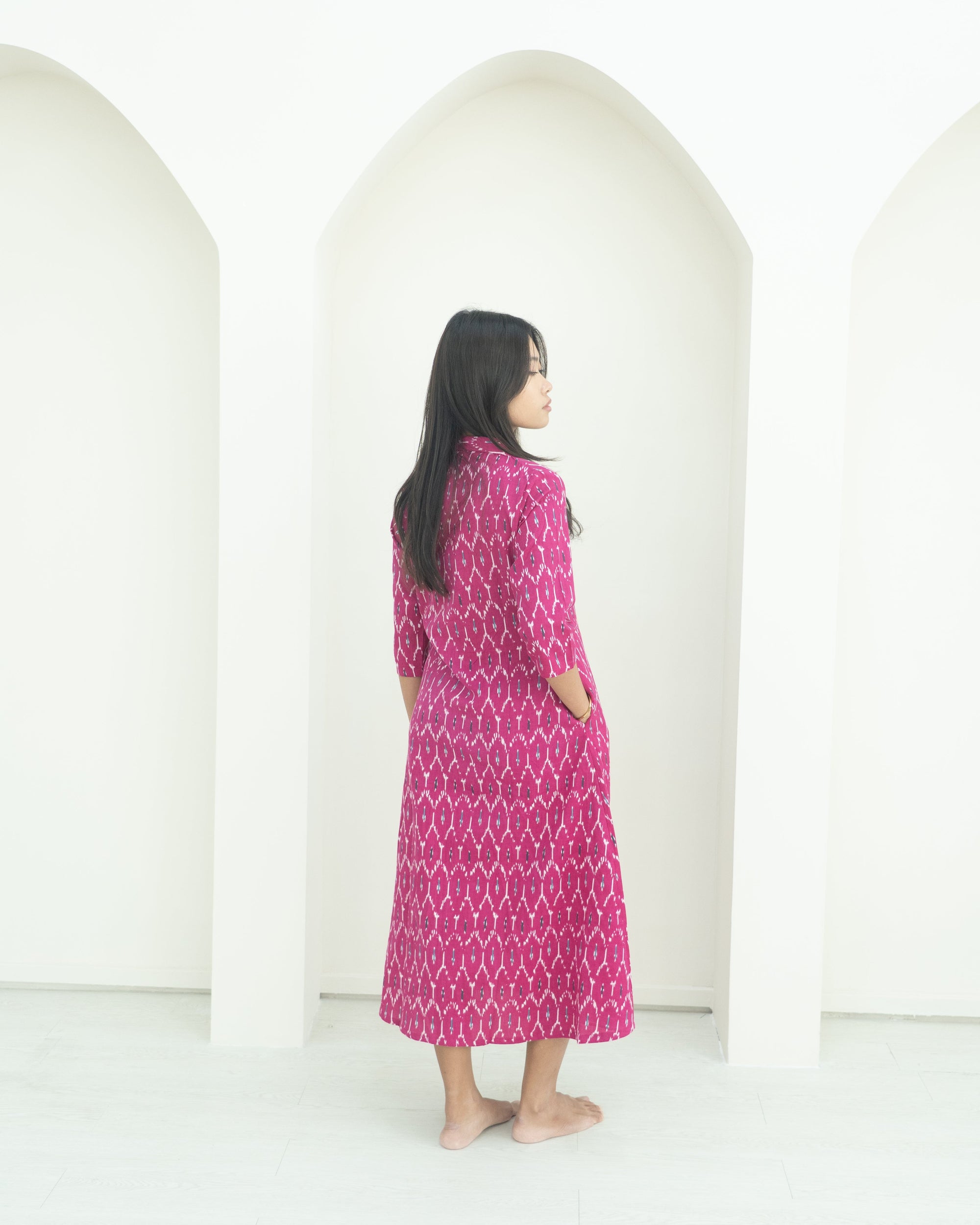 Woman wearing a pink patterned dress standing in front of white arches.