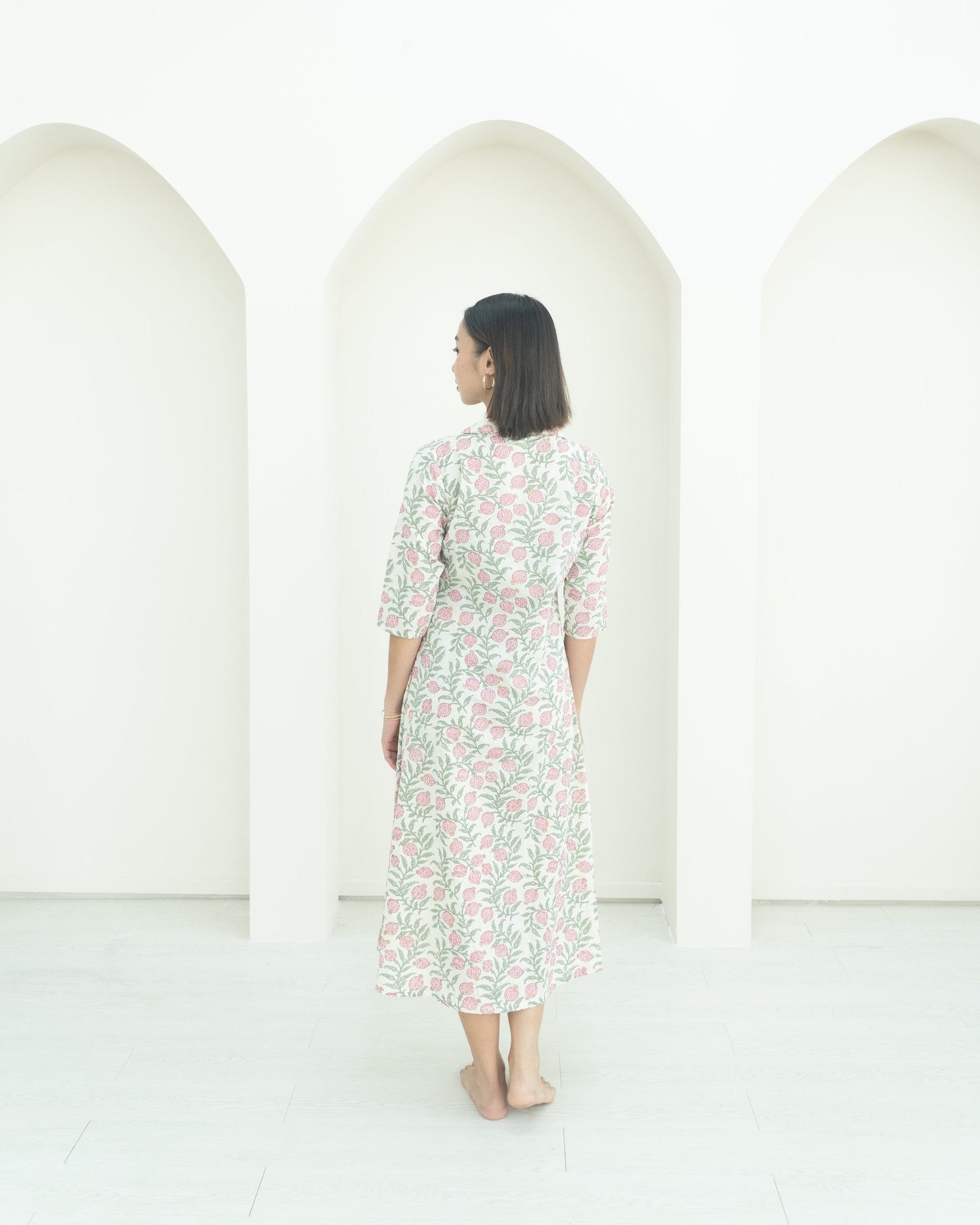 Woman in a floral dress standing in front of three white arches on a white background