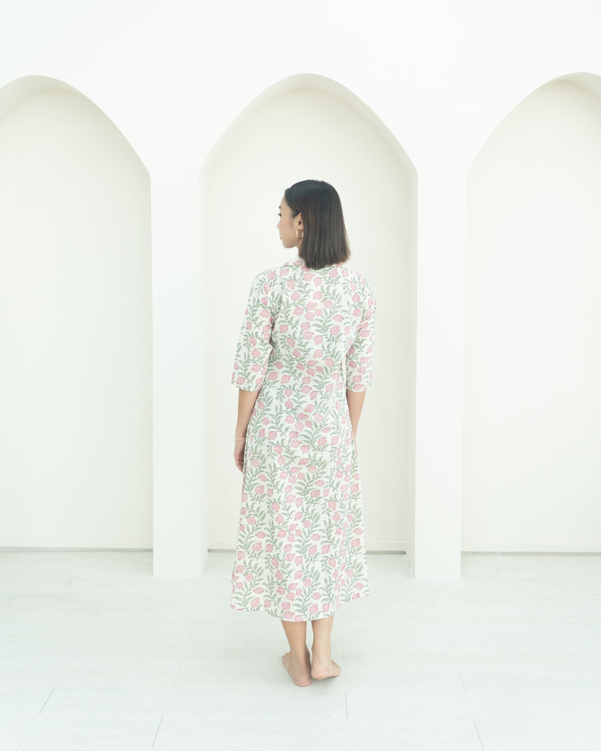 Woman in a floral dress standing in front of three white arches on a white background