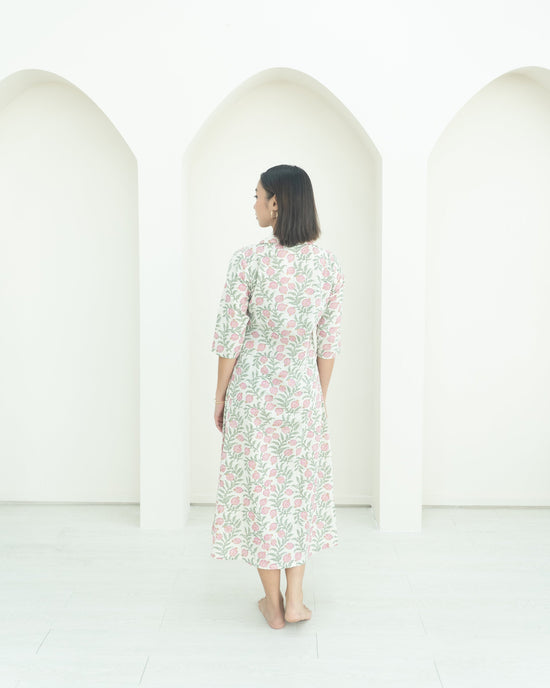 Woman in a floral dress standing in front of three white arches on a white background