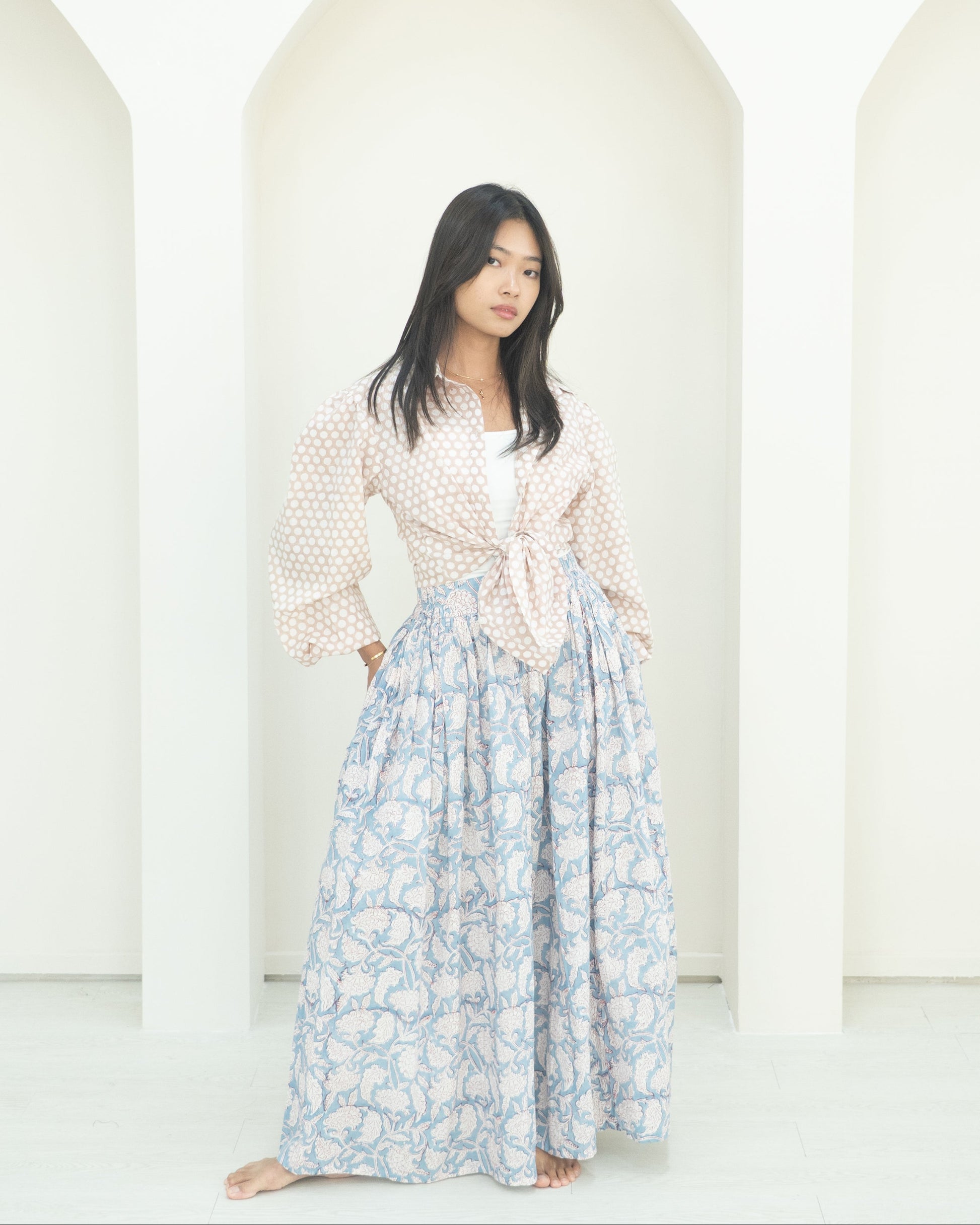 Woman wearing a light blouse and floral skirt against a white background
