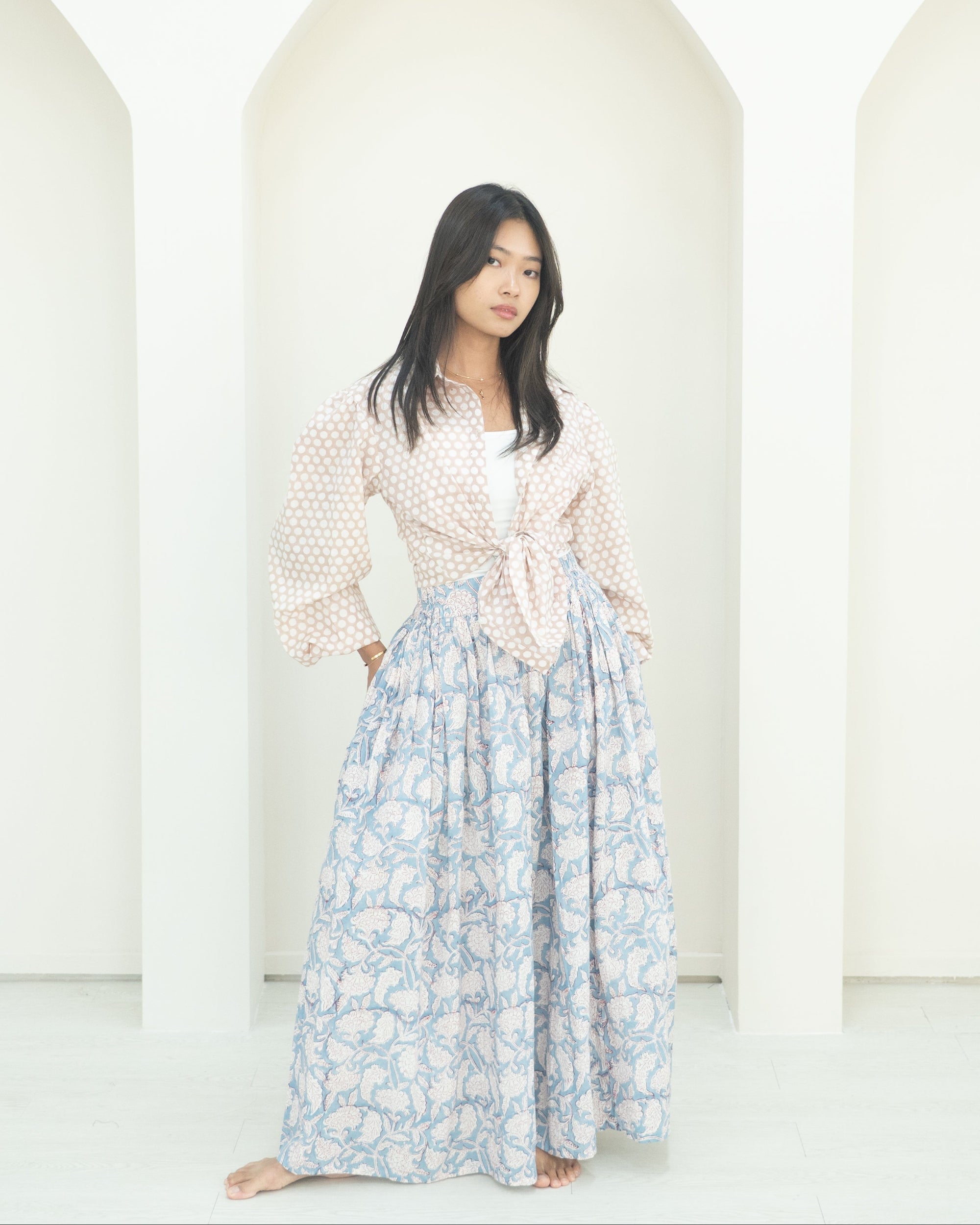 Woman wearing a light blouse and floral skirt against a white background