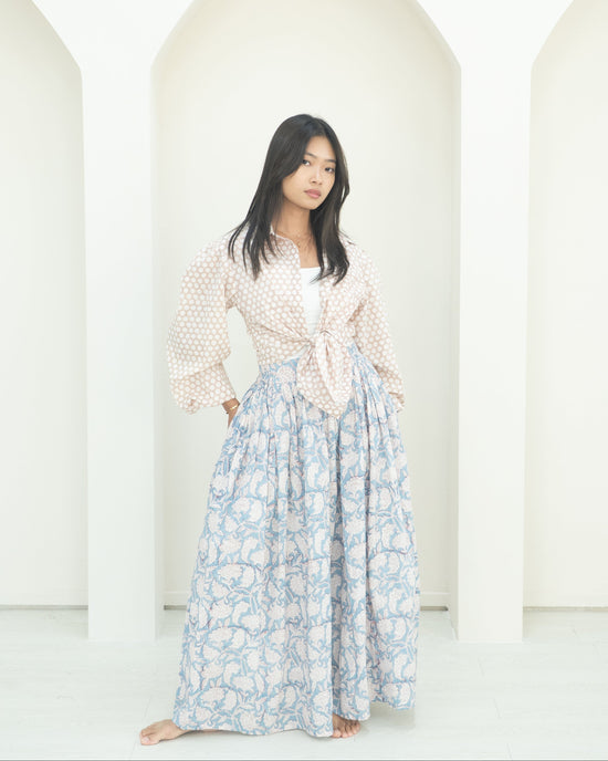 Woman wearing a light blouse and floral skirt against a white background