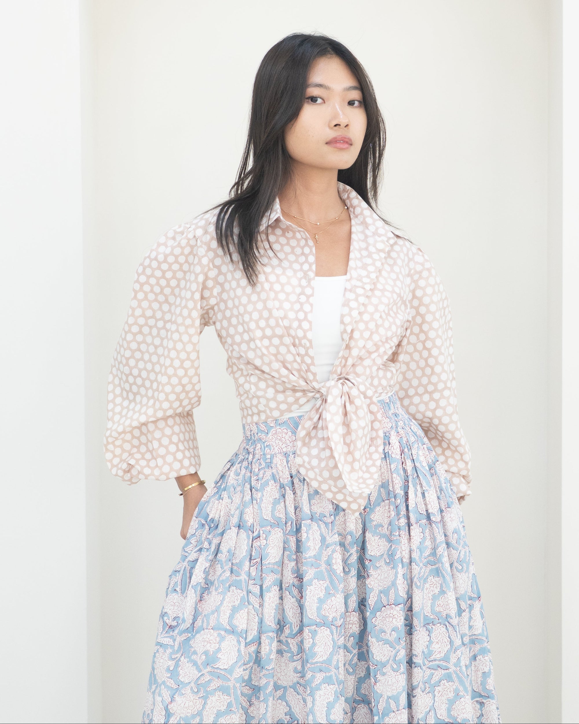 Woman wearing a polka dot blouse and floral skirt against a white background
