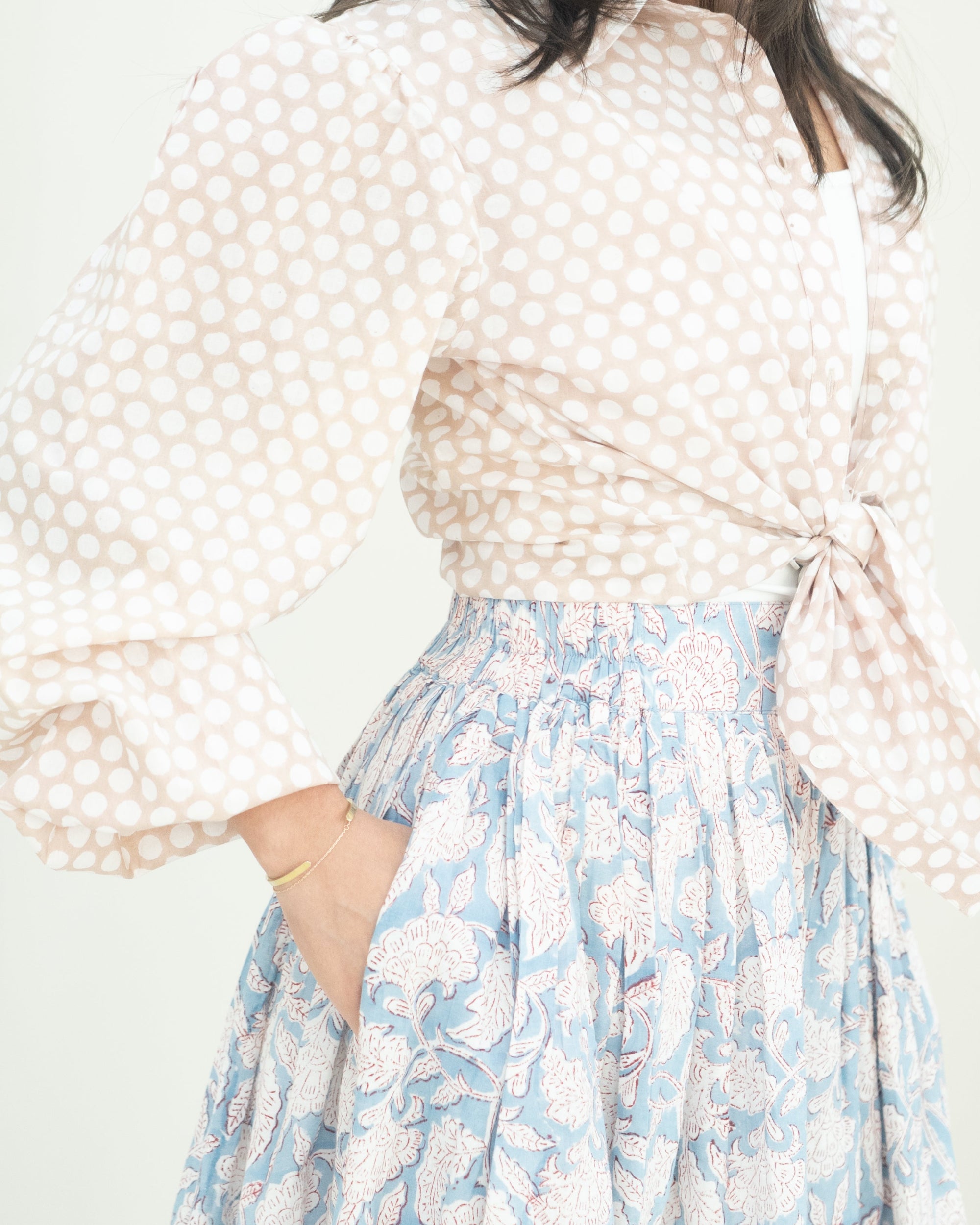 Woman wearing a polka dot blouse and floral skirt with a white background
