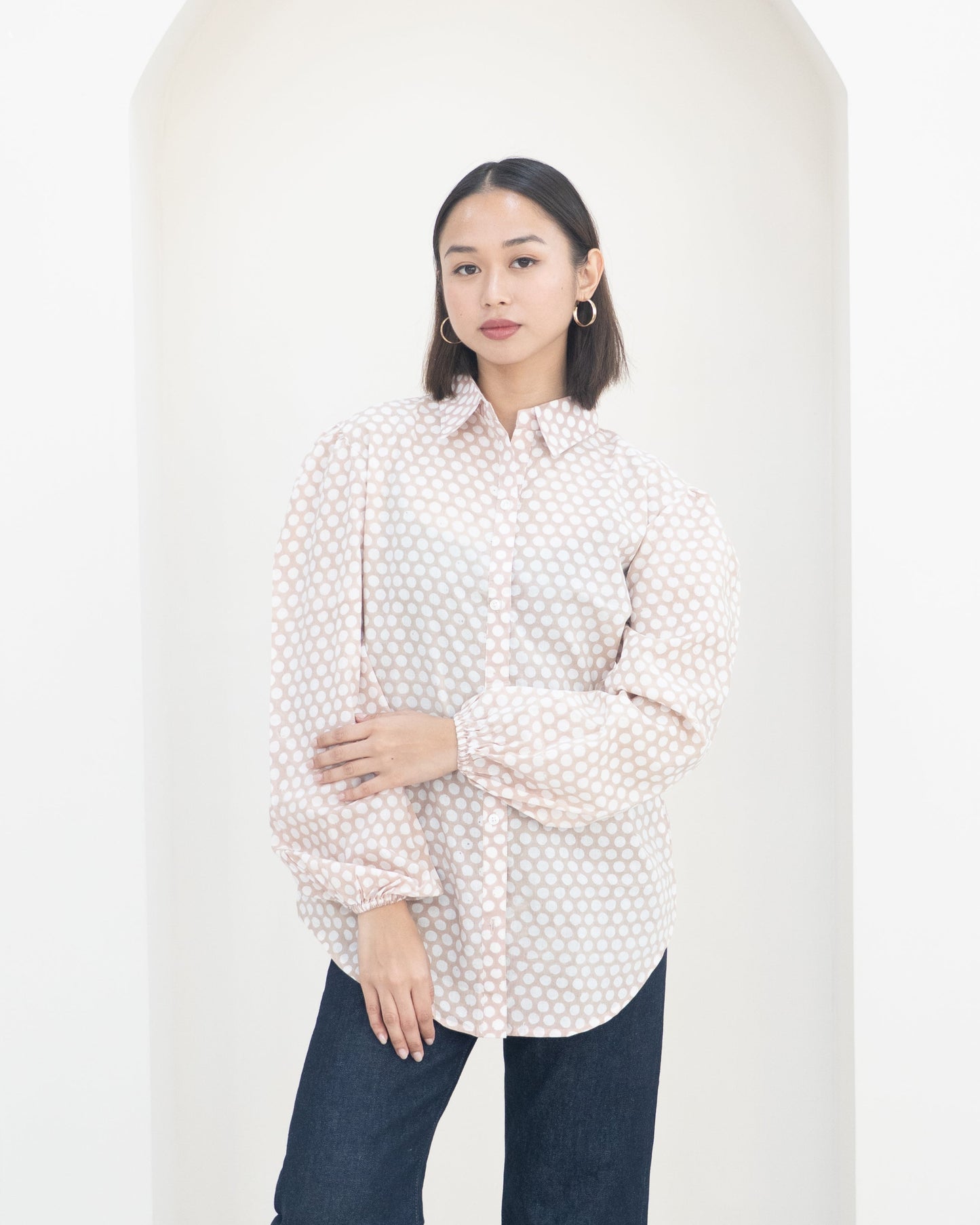 Woman wearing a polka dot blouse and dark pants against a white background