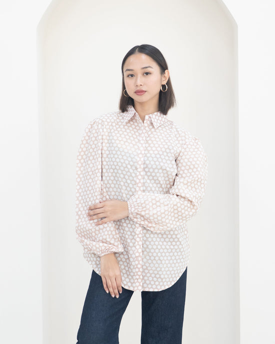 Woman wearing a polka dot blouse and dark pants against a white background