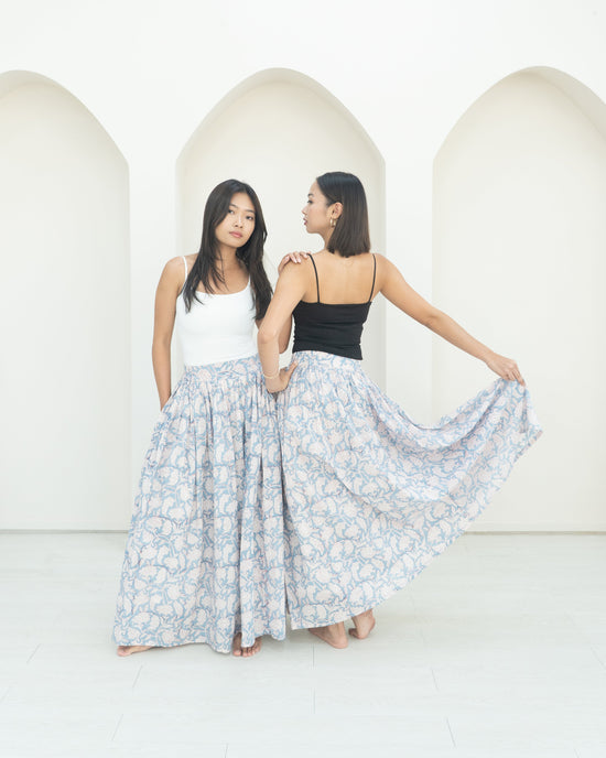Two women standing in front of a white wall with a floral skirt.