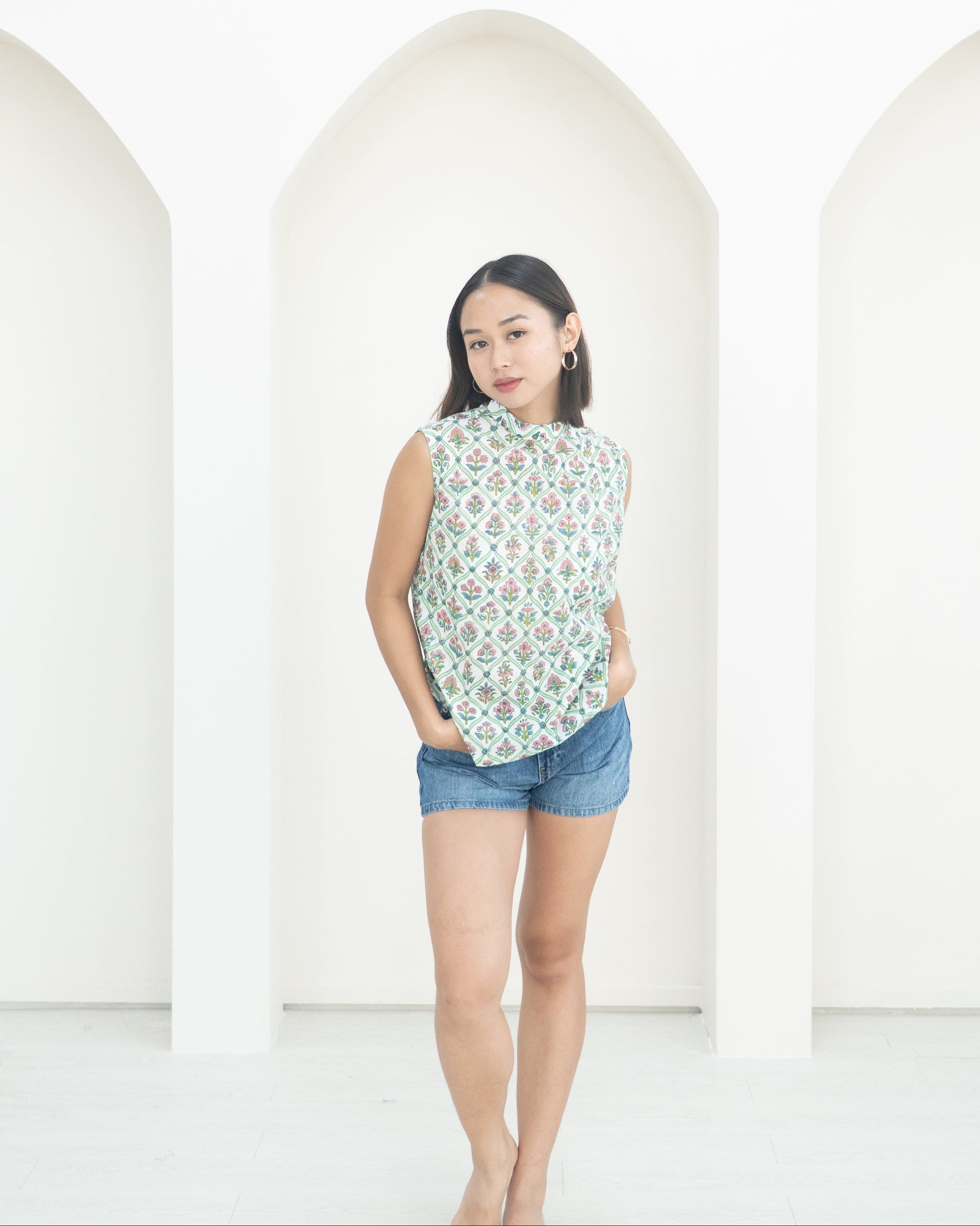 Woman wearing a sleeveless floral top and denim shorts against a white background