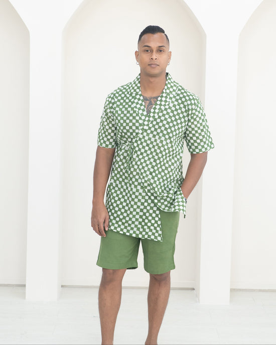Man wearing a green checkered shirt and shorts standing against a white background
