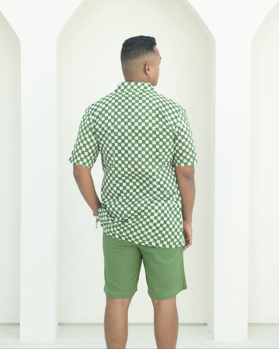 Man wearing a green checkered shirt and shorts standing against a white background