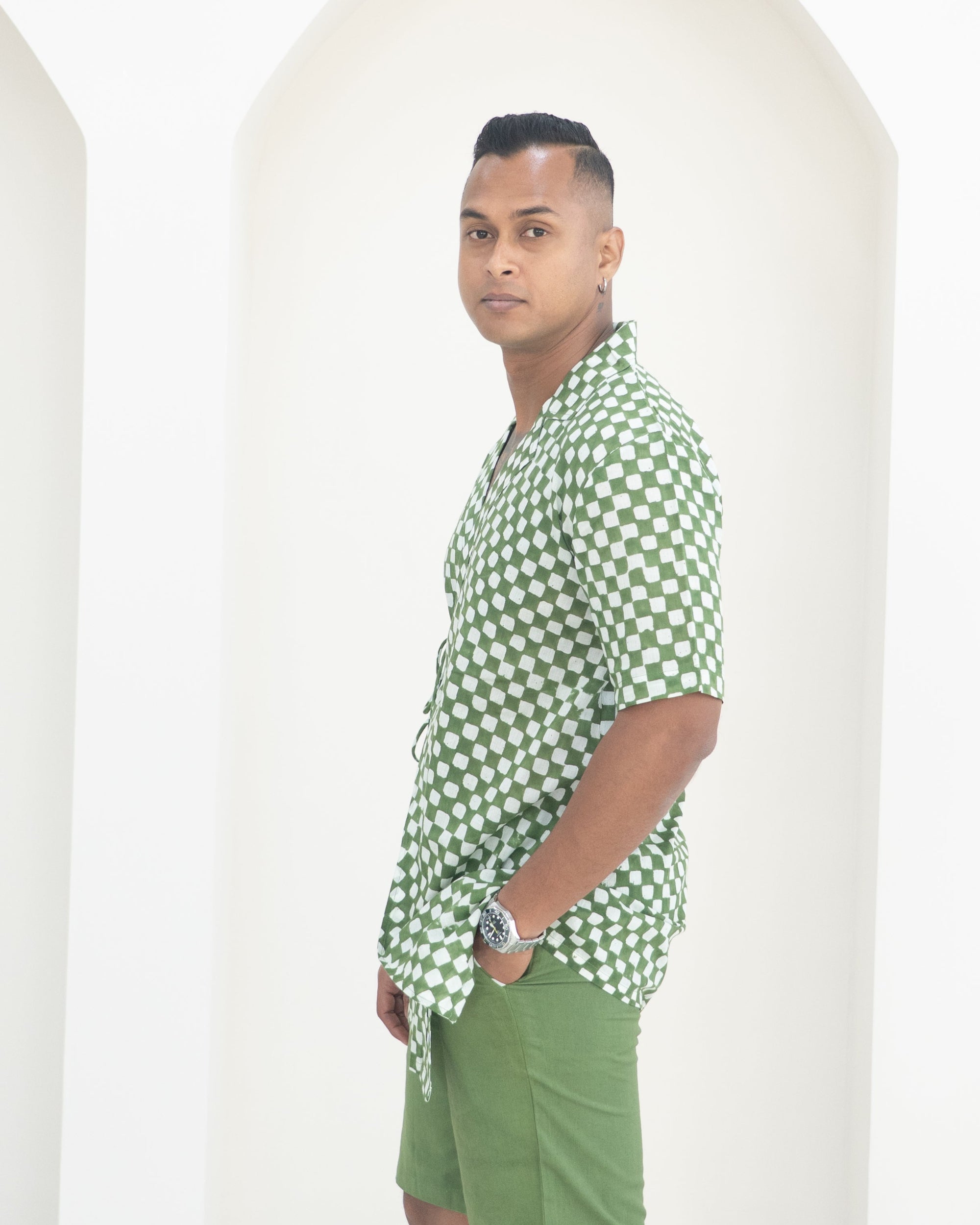 Man wearing a green and white checkered shirt and green shorts standing against a white background