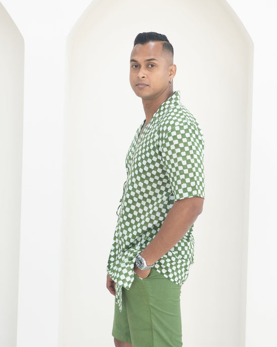 Man wearing a green and white checkered shirt and green shorts standing against a white background