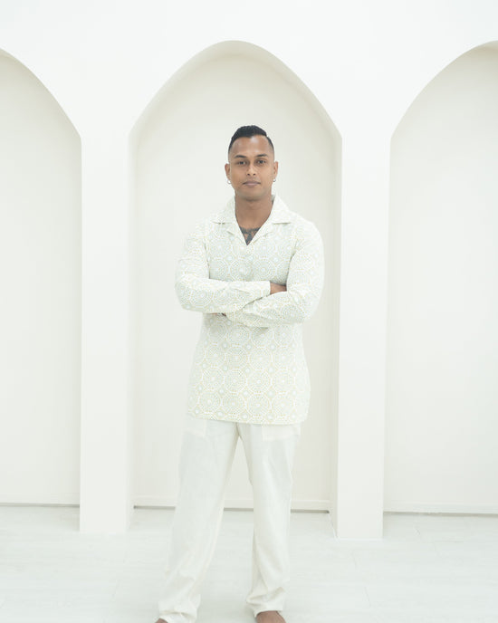 A man wearing a white patterned shirt and matching trousers.