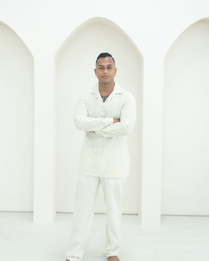 A man wearing a white patterned shirt and matching trousers.