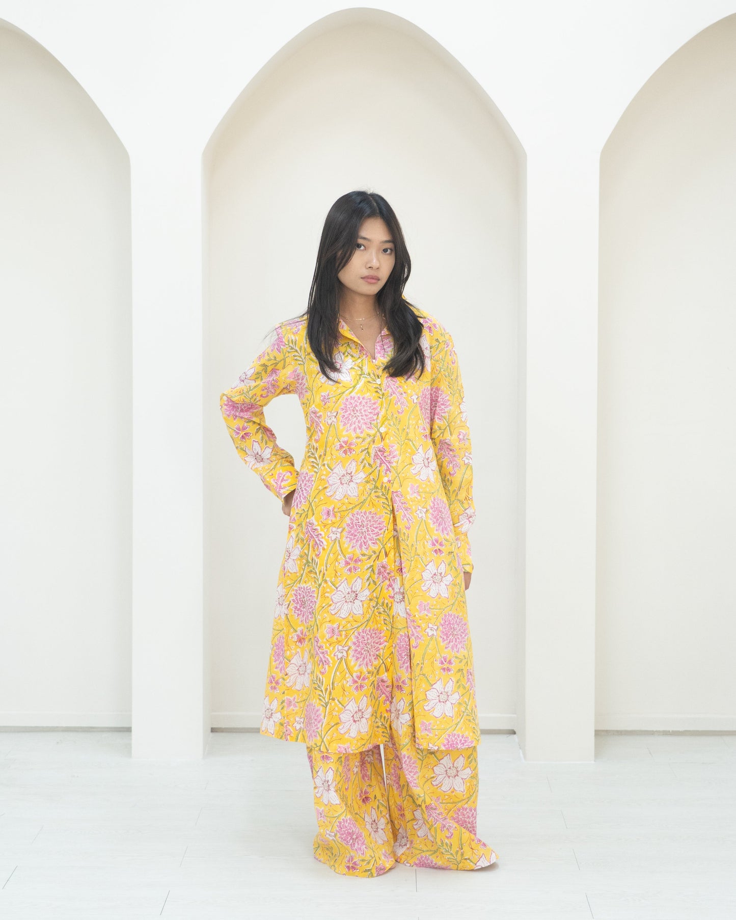 Woman in a yellow floral outfit standing in front of white background