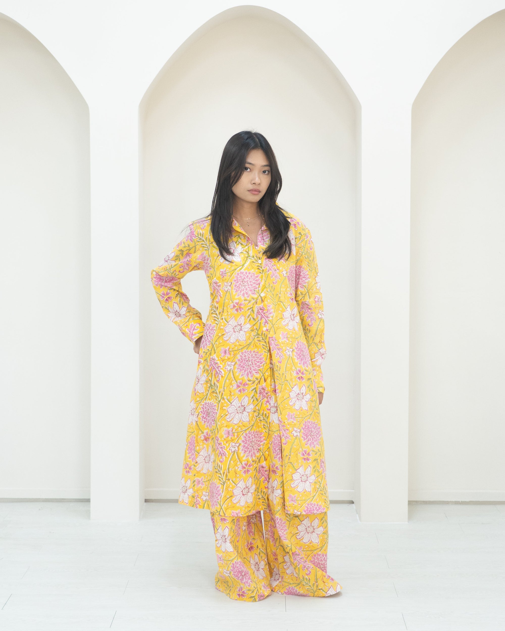 Woman in a yellow floral outfit standing in front of white background