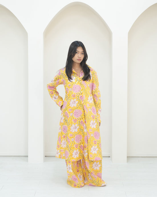 Woman in a yellow floral outfit standing in front of white background