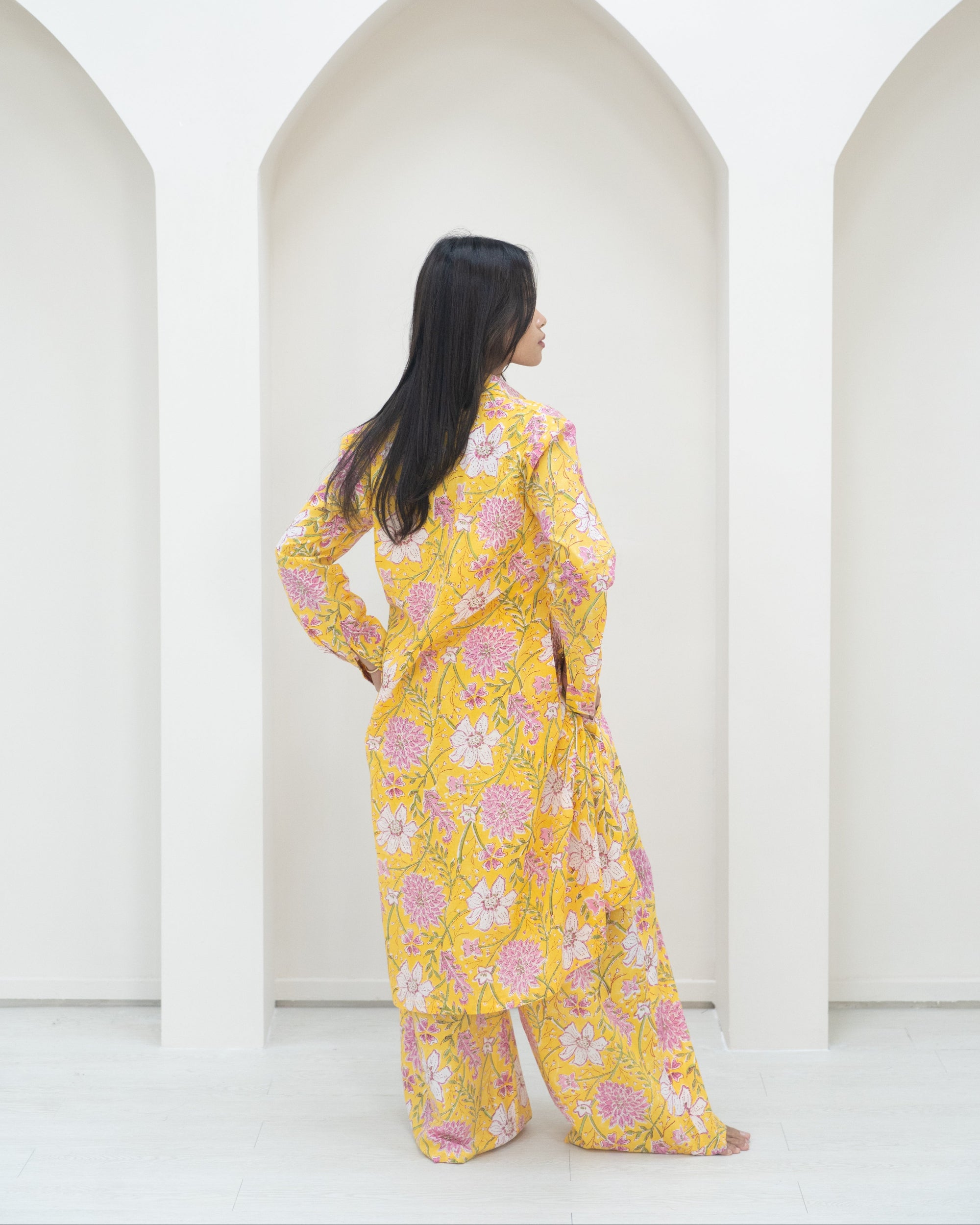 Woman in a yellow floral outfit standing in front of white background