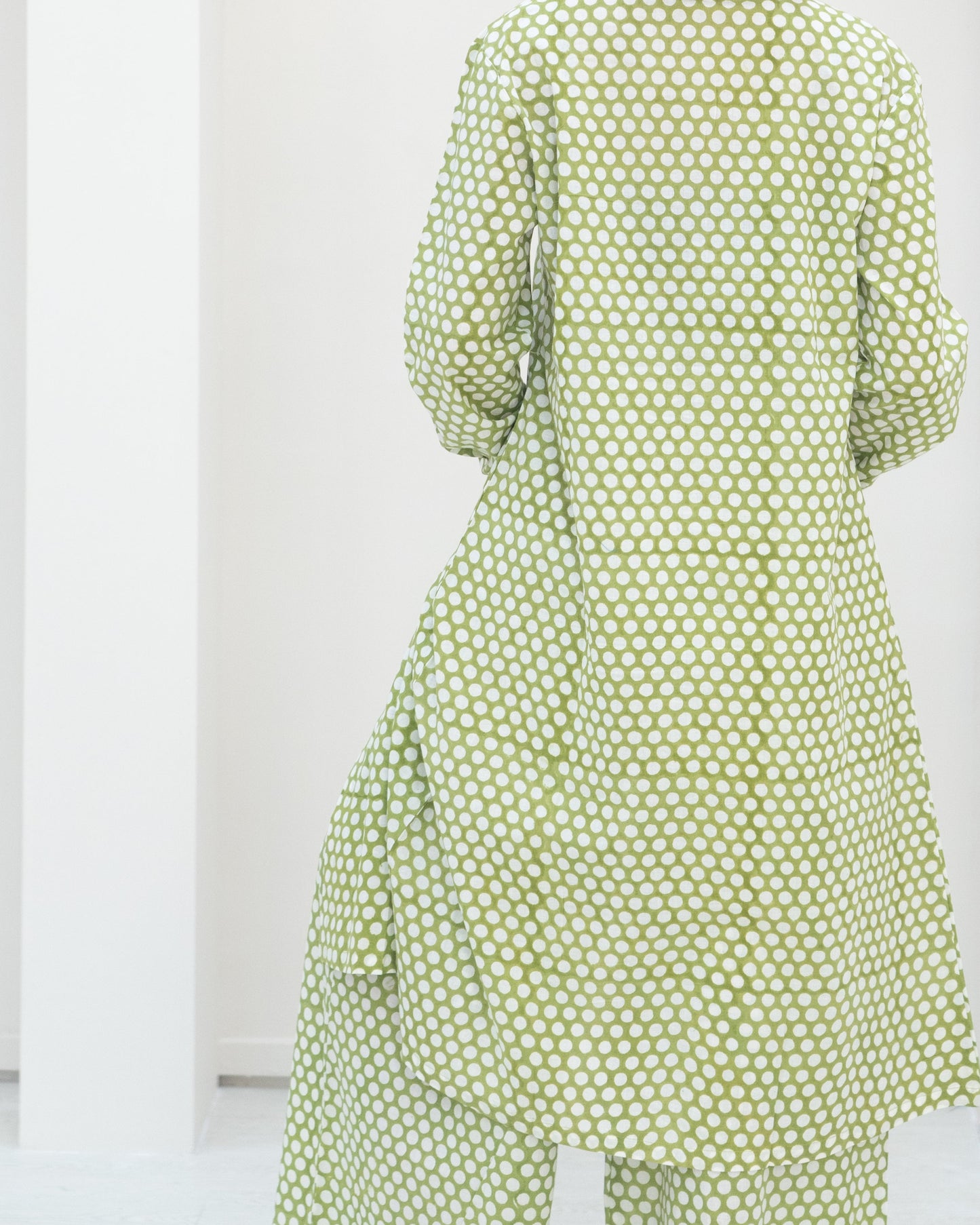 Person wearing a green polka dot dress against a white background