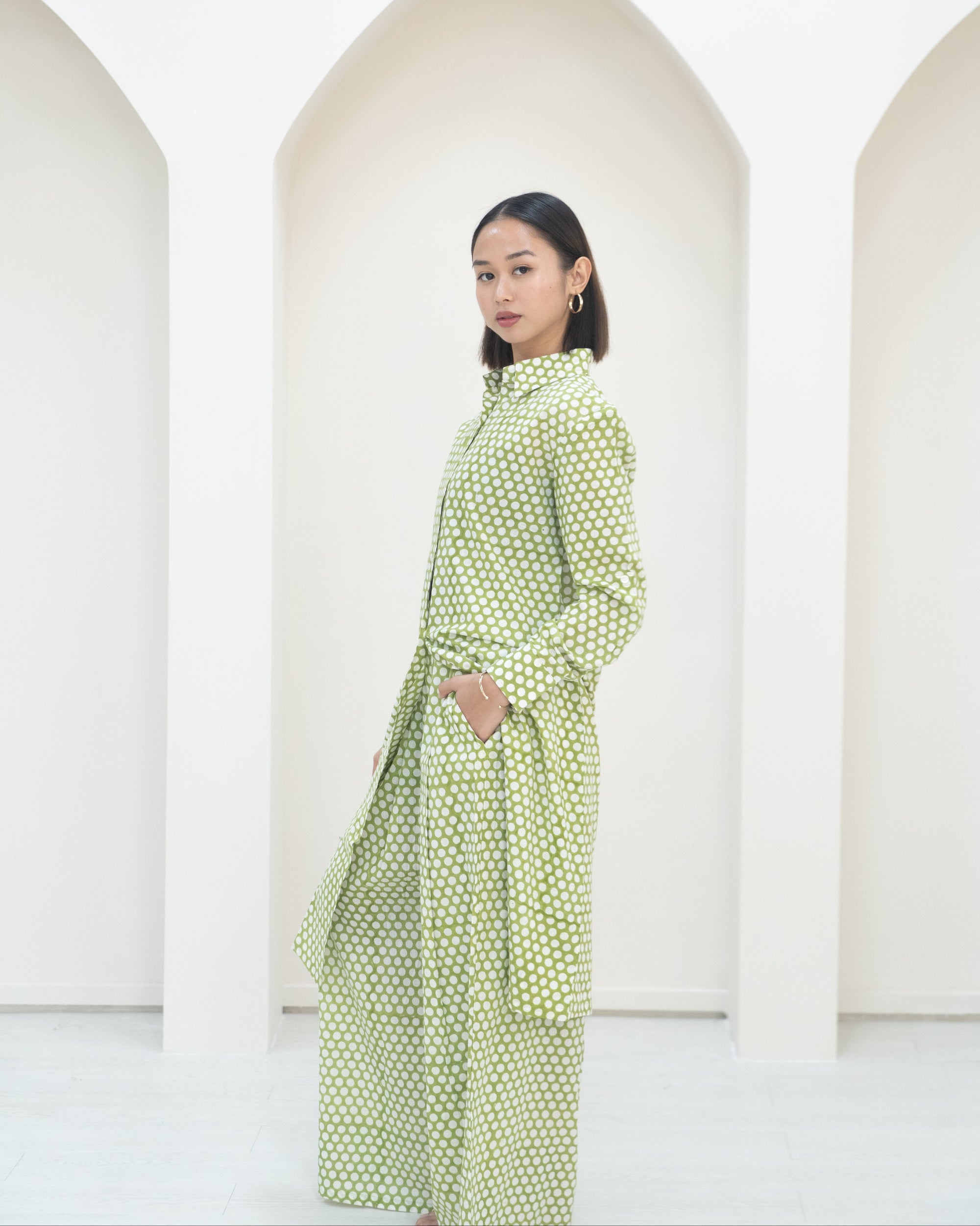 Woman wearing a green polka dot dress standing against a white background