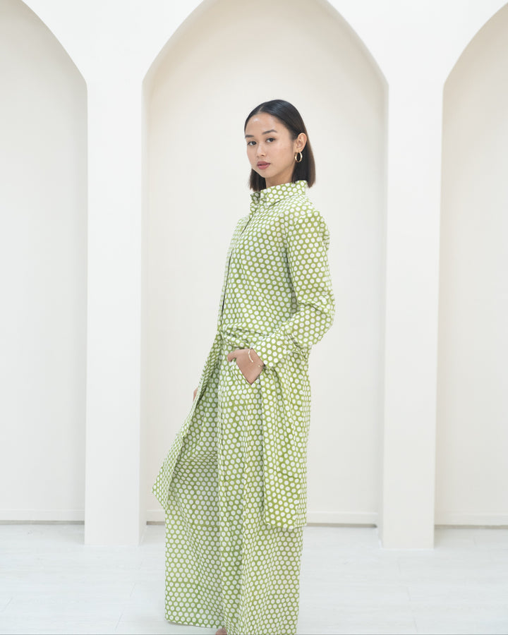 Woman wearing a green polka dot dress standing against a white background