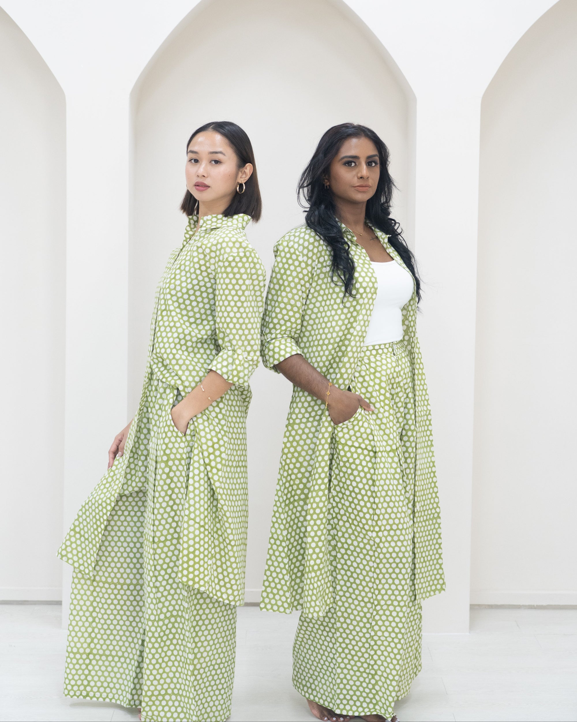 Two women wearing green polka dot outfits standing in front of white background