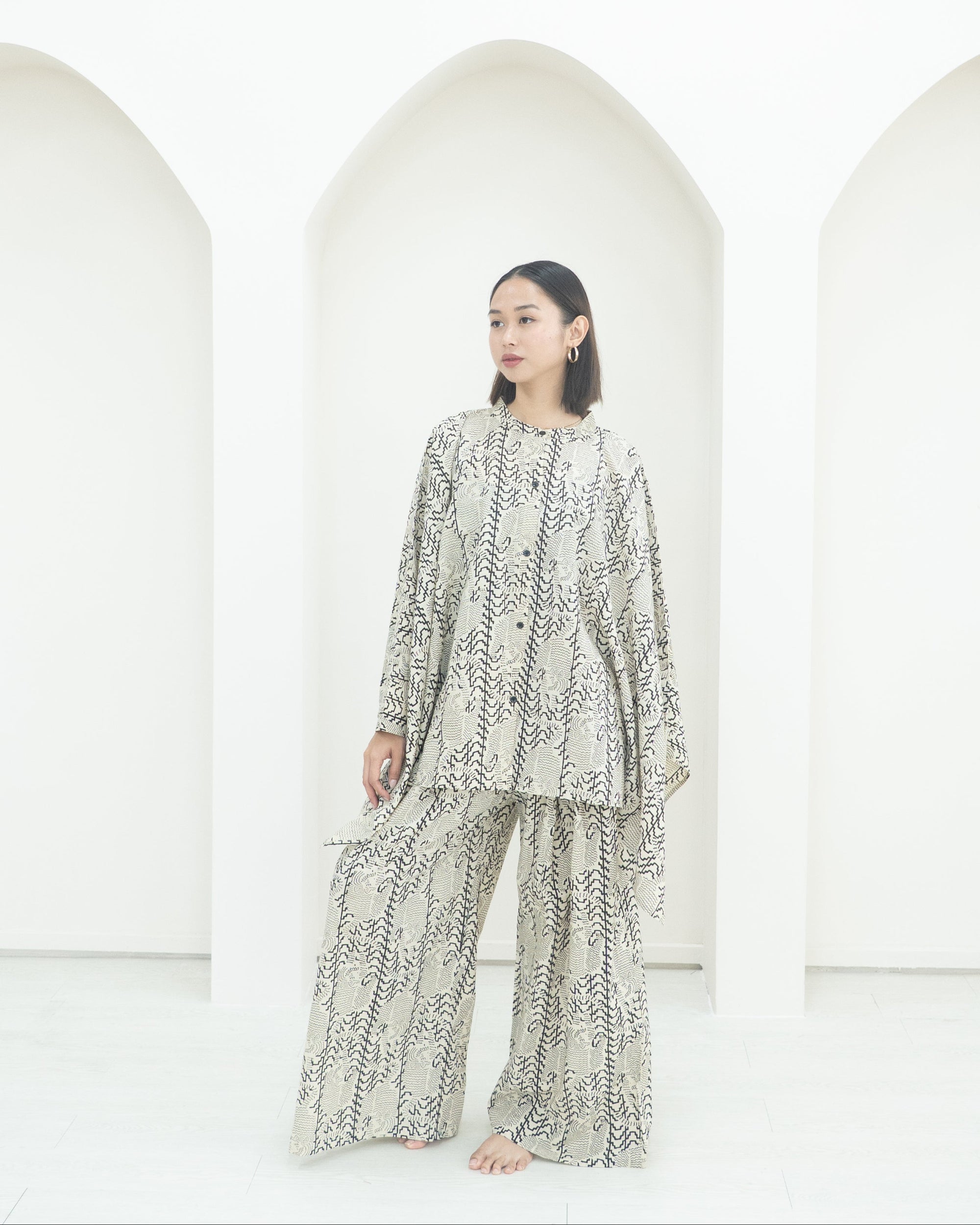 Person wearing a patterned outfit standing in front of white arches.
