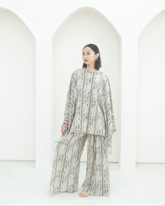 Person wearing a patterned outfit standing in front of white arches.