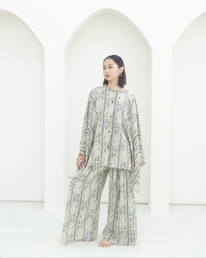 Person wearing a patterned outfit standing in front of white arches.
