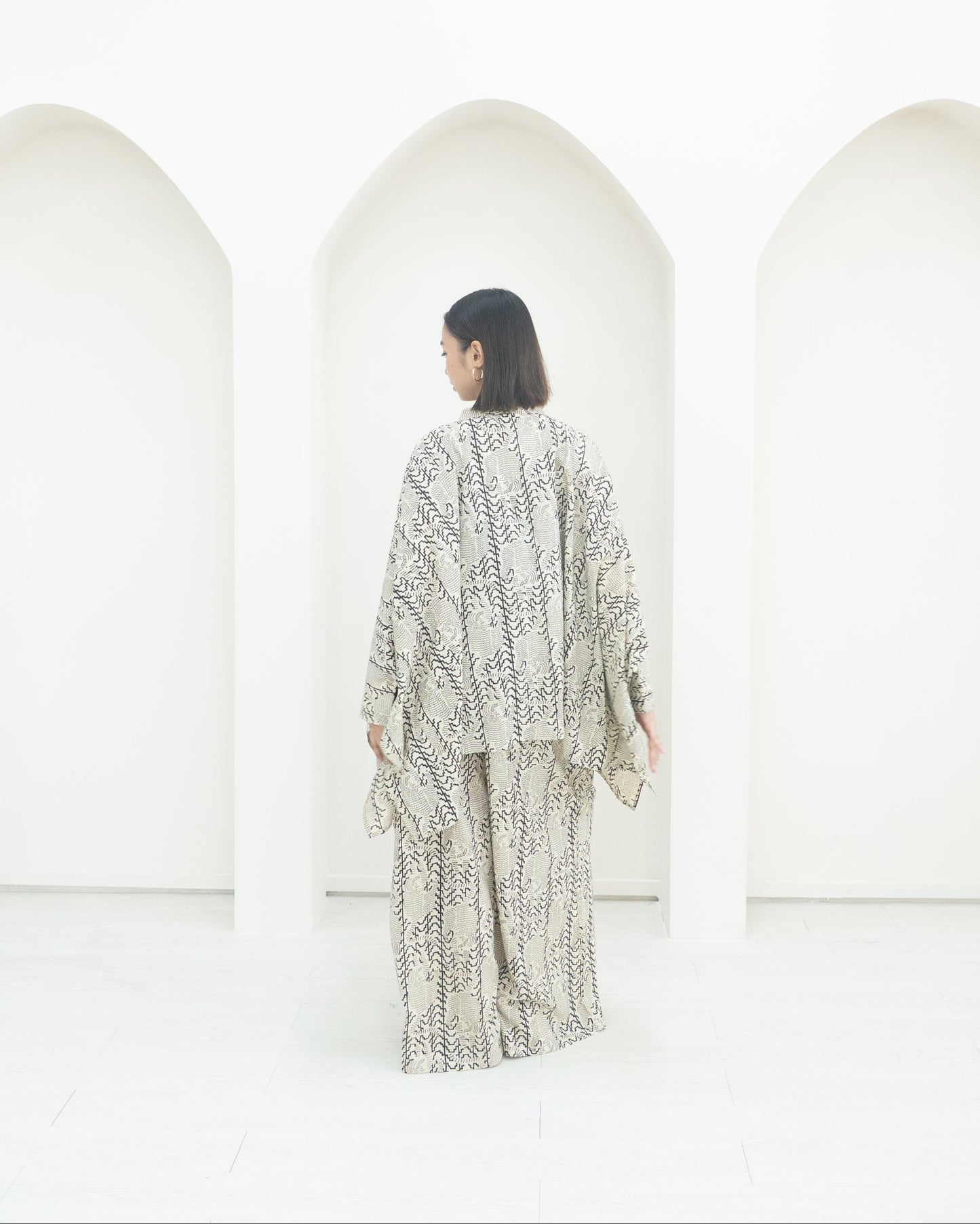 Person wearing a patterned outfit standing in front of white structures.