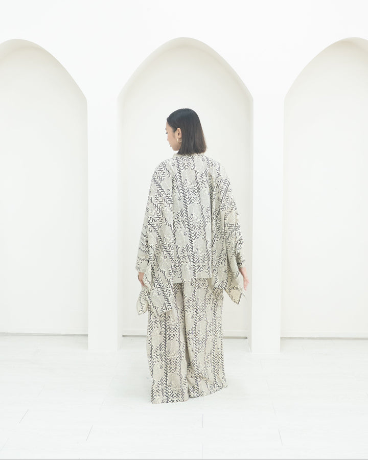 Person wearing a patterned outfit standing in front of white structures.