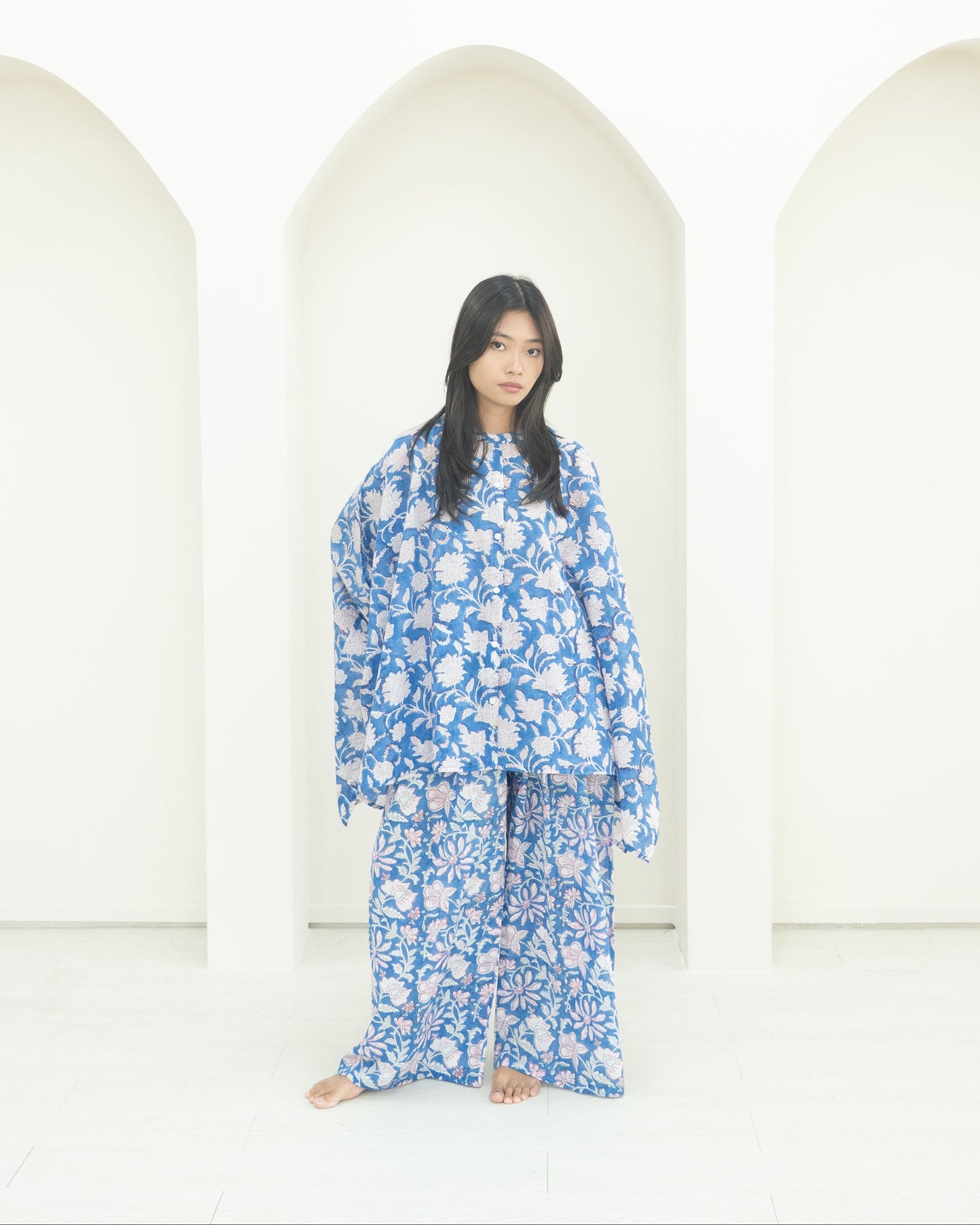 Person wearing a blue floral outfit standing in front of white arches.
