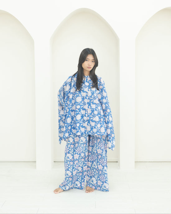 Person wearing a blue floral outfit standing in front of white arches.