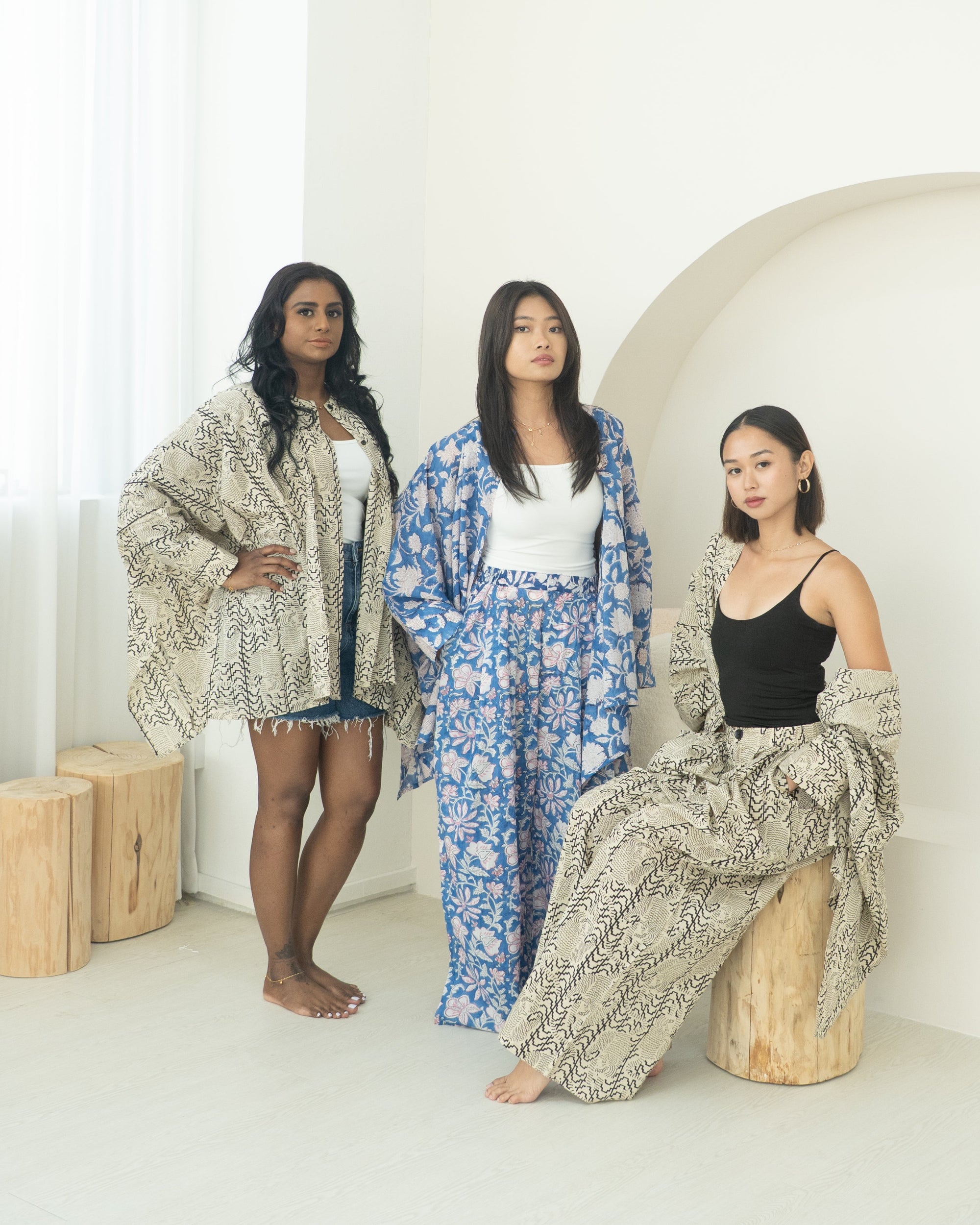 Three women in stylish outfits standing in a minimalistic room with white walls.