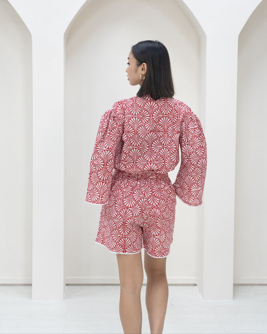 Person wearing a red and white patterned outfit standing against a white background