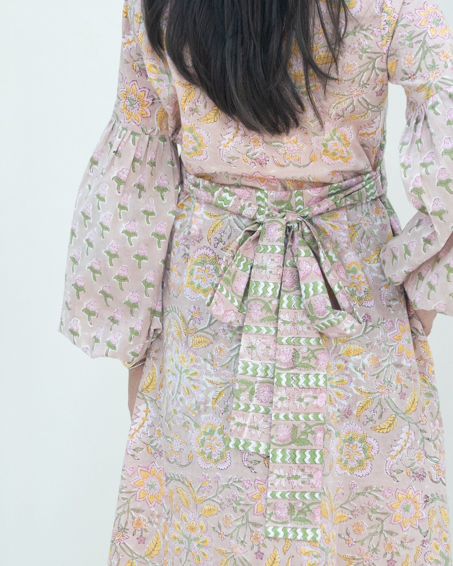 Person wearing a floral dress with a green belt on a light background