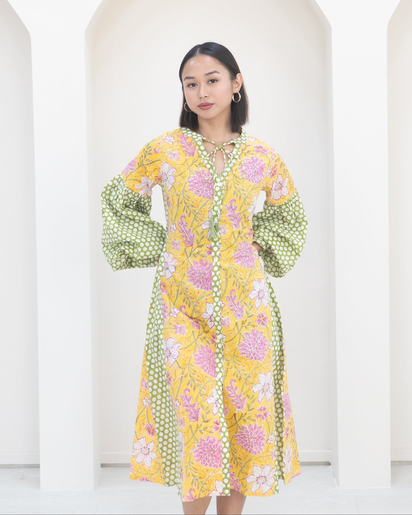Woman wearing a yellow floral dress with green polka dot sleeves against a white background
