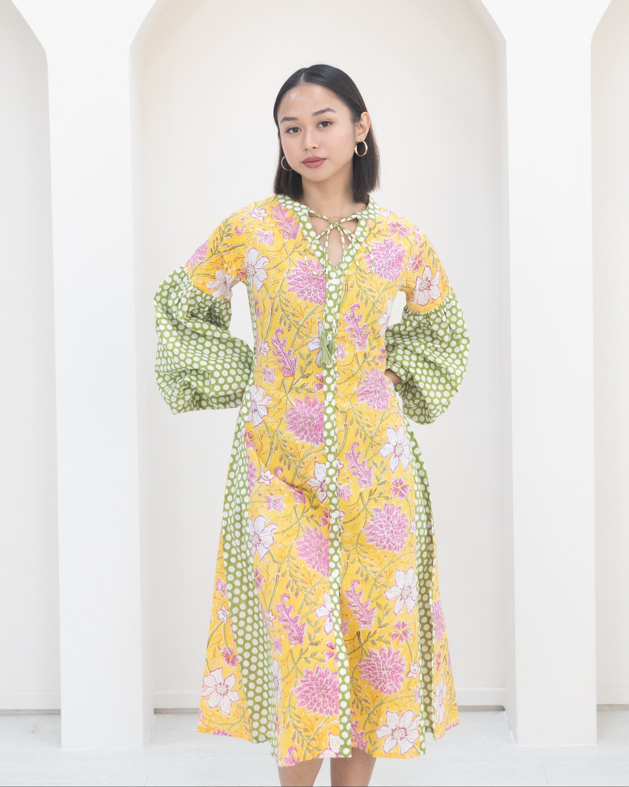 Woman wearing a yellow floral dress with green polka dot sleeves against a white background